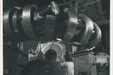 One of 24 magnetic coils being moved into position on the CLEO device at Culham Laboratory to produce a stellarator configuration.
The field from these coils with the field produced by currents flowing through the helical conductors around the torus (in the foreground) provides the confining magnetic field for high temperature plasma.
(IAEA Archives/Credit: UKAEA, United Kingdom)